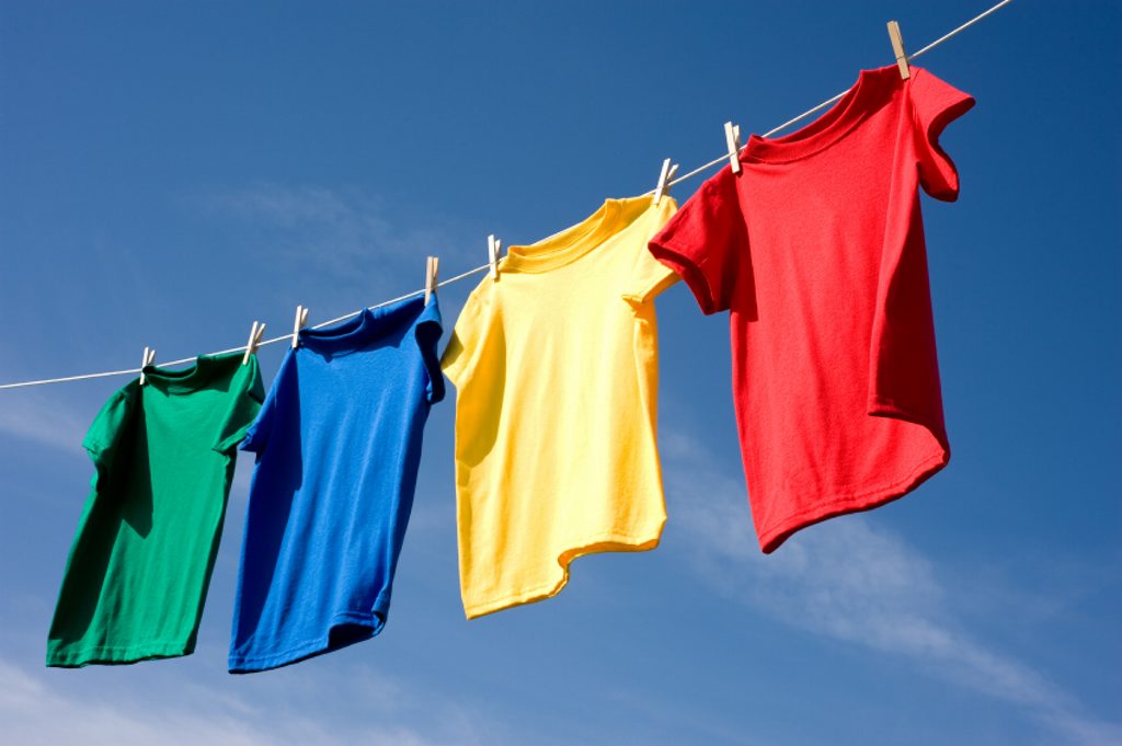 a set of primary colored T-shirts hanging on a clothesline on a beautiful, sunny day, add text or graphic to shirts or copy space a set of primary colored T-shirts hanging on a clothesline on a beautiful, sunny day, add text or graphic to shirts or copy space